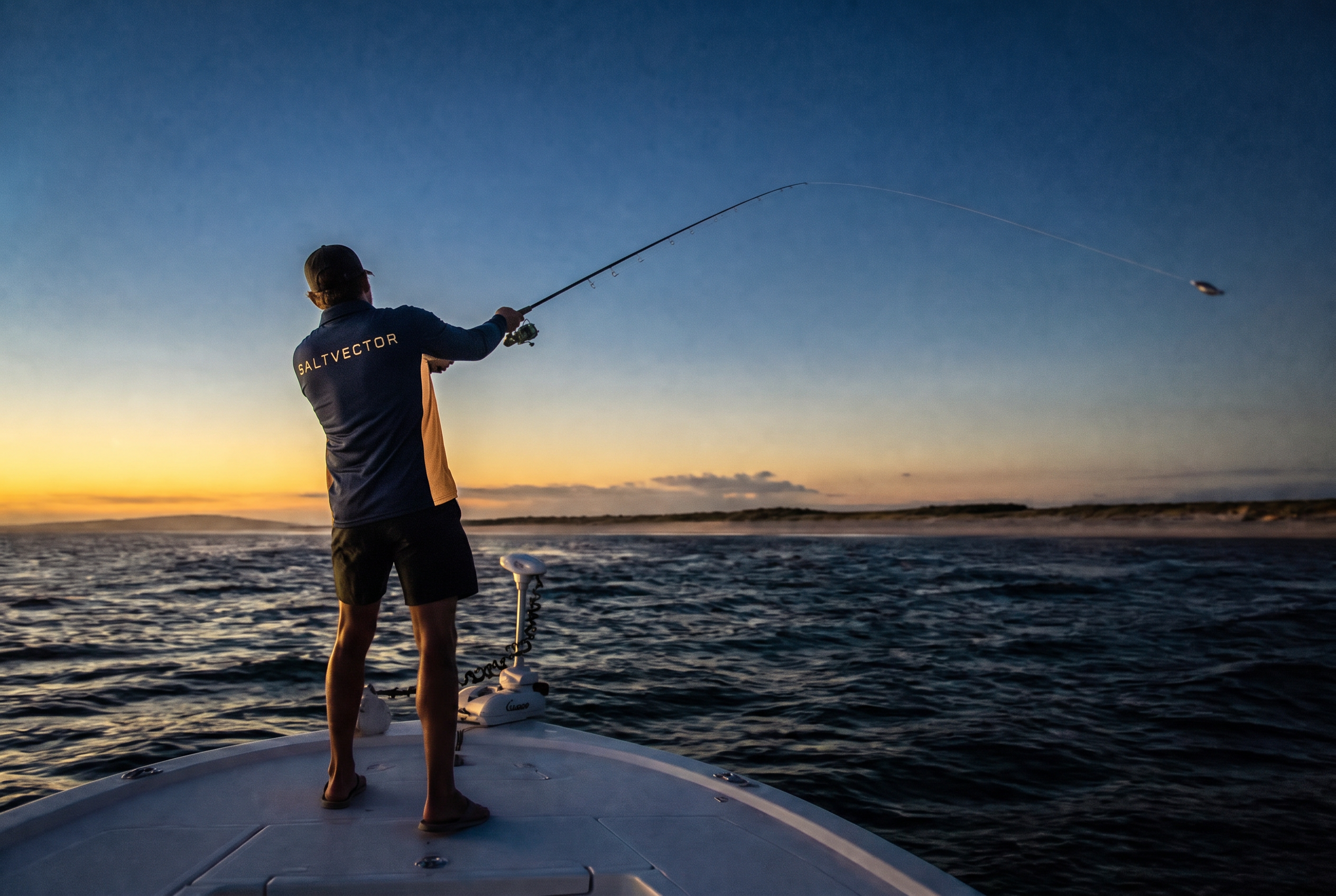Angler wearing the navy and sand SaltVector fishing shirt casting from a boat at sunset